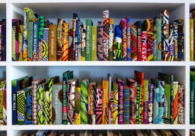Yinka Shonibare MBE, “The British Library” (2014), hardback books, Dutch wax printed cotton textile, gold foiled names, table with benches, four iPads, iPad stands, headphones, interactive application (Courtesy the artist and James Cohan Gallery, New York; Photo: Phoebe D’Heurle)